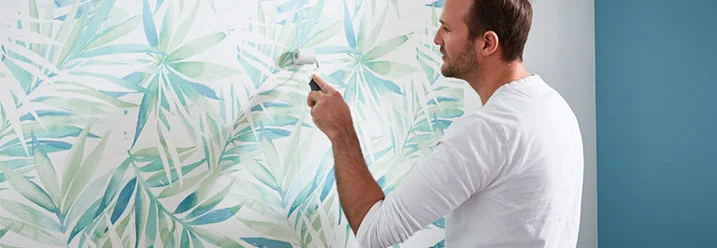 Person bringt Tapete mit Blättern an